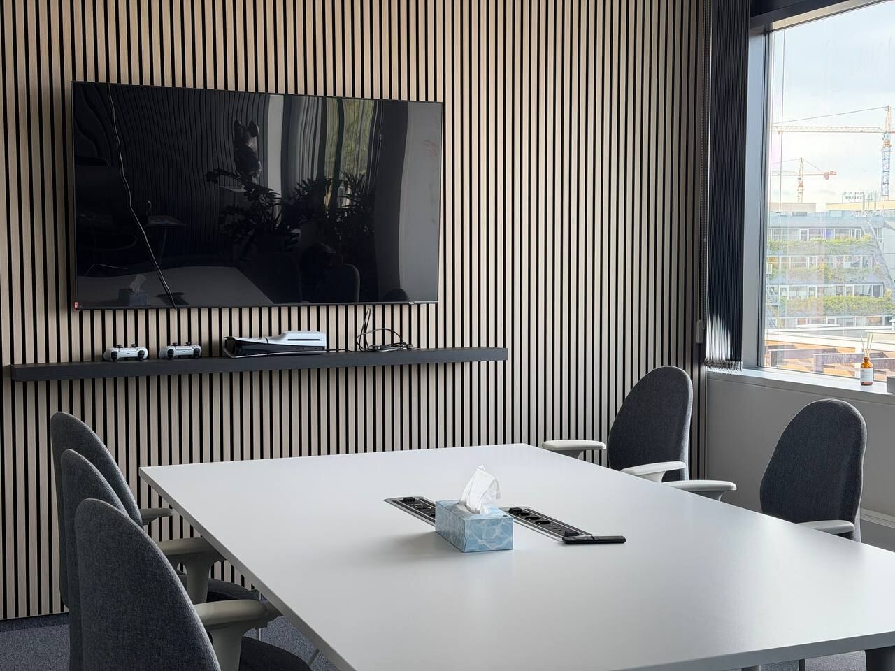 Meeting room with a TV screen, table, six chairs and a slatted wall