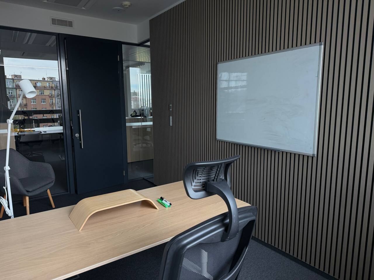 Desk in a private office with a slatted wall, whiteboard and floor lamp
