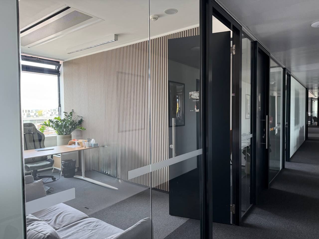 Private office behind a glass wall with a desk, chair, plant and sofa